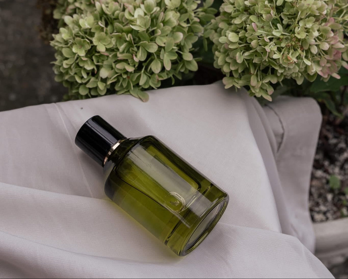 Artisan of Sense botanical body and room mist in olive green glass bottle with black cap on draped linen with green hydrangeas