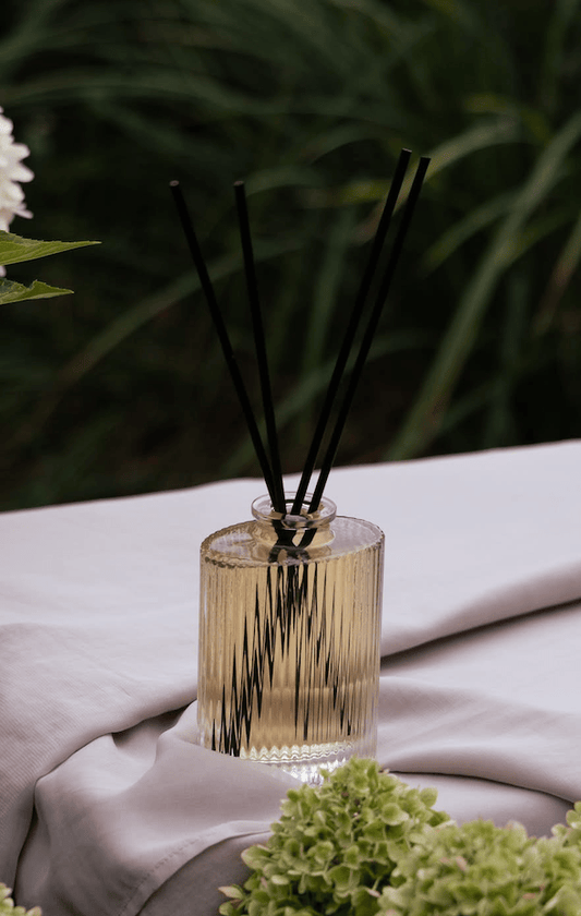 Clear fluted glass reed diffuser holding pure essential oil room fragrance with its slim black diffuser reeds. Handcrafted alcohol-free aromatherapy diffuser range by Artisan of Sense Singapore, formulated without DPG or phthalates for continuous non-toxic home scenting and luxury interior styling.